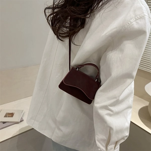Petit sac carré bordeaux minimaliste avec poignée porté sur une chemise blanche