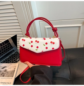 Detail of red and white shoulder bag featuring cherry pattern and knot handle decoration