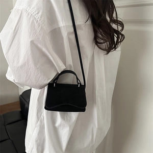 Petit sac bandoulière noir mat avec boucle argentée porté sur une chemise blanche