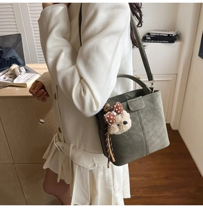 Olivgrüne Beuteltasche kombiniert mit weißem Blazer und niedlichem Bären-Anhänger-Detail