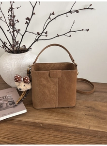 Detailaufnahme einer braunen Wildleder-Beuteltasche mit niedlichem Plüschbär-Anhänger