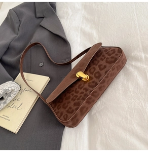 Detail of leopard print suede underarm bag with gold twist lock on white fabric