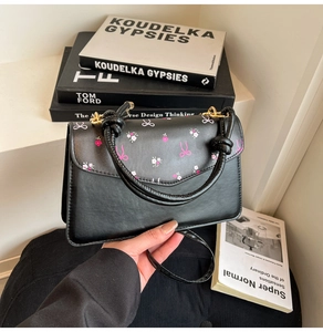 Detail of black faux leather handbag with pink floral ribbon and twisted rope handle