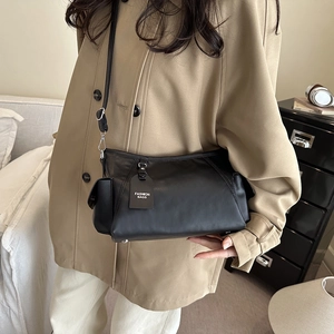 Minimalist black matte leather crossbody bag with adjustable strap and decorative tag