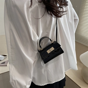 Mini sac carré en cuir verni noir avec boucle dorée porté par un mannequin