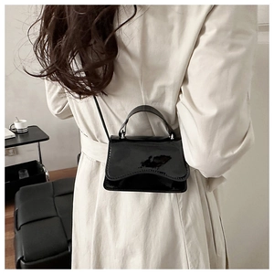 Mini black patent leather crossbody bag with top handle shown on a model