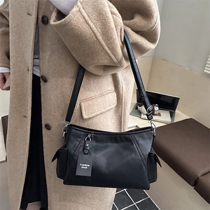 Minimalist black leather shoulder bag with side pockets shown in a stylish lifestyle setting