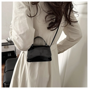Rear view of a black patent leather mini crossbody bag with a curved flap design