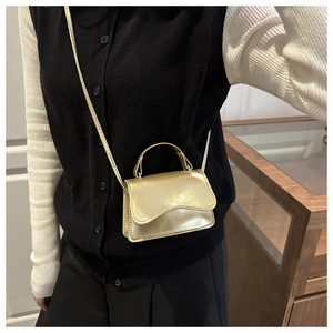Detail of a mini gold crossbody bag with metallic top handle and glossy finish on a model
