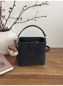Detail der schwarzen matten Lederbeuteltasche mit Griff und süßem Bärenanhänger auf Tisch