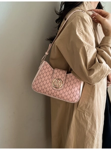 Pink underarm bag with M-pattern print and gold clasp shown on a beige trench coat