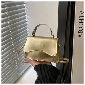 Detailed view of golden metallic handbag with wavy edge lid and adjustable shoulder strap