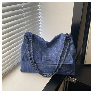 Detail der blauen Denim-Umhängetasche mit Metallstab und gewebtem Kettenriemen