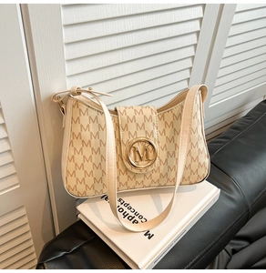 Close-up of beige monogram shoulder bag with gold M-logo on a white book display