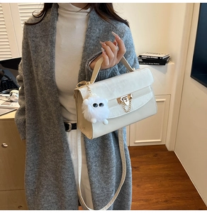 Chic beige leather square bag with gold lock and plush charm on a grey cardigan model