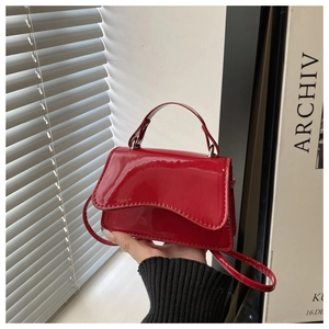 Detail of red patent leather mini handbag with top handle and slender shoulder strap