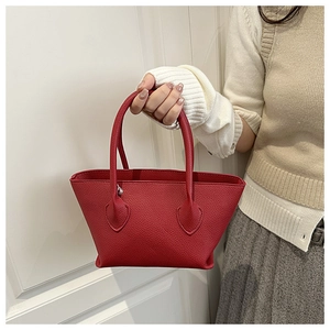 Detail of red pebbled leather tote bag held by model wearing a pleated skirt