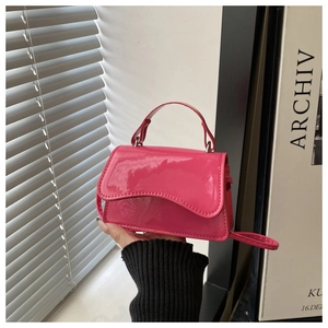 Close-up of a mini bright pink patent leather handbag with a circular handle and thin strap