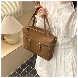 Detail of brown leather tote bag featuring dual front zipper pockets and white stitching