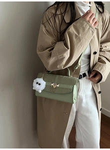 Detail of light green square bag with gold rivet lock and white plush monster charm