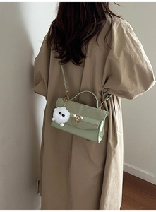 Detail of light green crossbody bag with gold lock, chain strap and plush ball charm