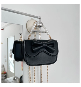 Close-up of black crossbody bag featuring a large bow, pearl handle, and gold chain strap