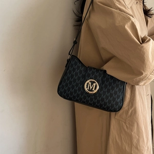 Chic black monogram shoulder bag with gold logo emblem on a minimalist trench coat background