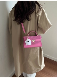 Detail of pink crossbody bag with pleated flap, gold clasp, and white plush charm