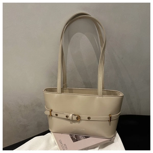 Detail of beige tote bag with gold buckle elements on white knitted background