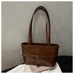 Close-up of deep brown leather tote bag with gold metal buckle and thin decorative belt