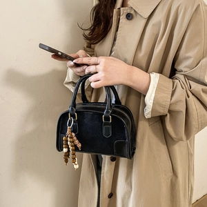 Minimalist black matte leather Boston handbag with ethnic wood bead charm on trench coat model