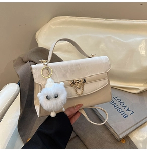 Detail of a creamy white flap handbag with gold rotating lock and cute pompom charm