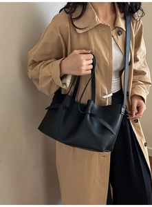 Detail of black tote bag with decorative side knots and slim straps on khaki trench coat
