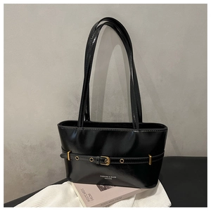 Detail of black glossy patent leather tote with gold buckle and brand logo on white fabric