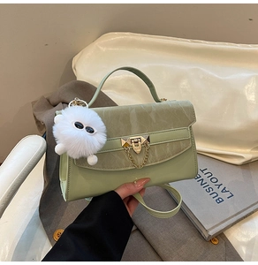 Detail of light green crossbody bag featuring a golden twist lock and plush white charm