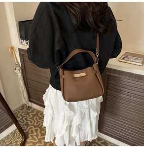 Detail view of dark brown pebbled leather bucket bag with gold clasp and long strap