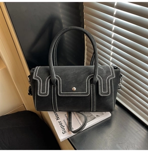 Detail view of black handbag featuring contrast white stitching and metal snap closure