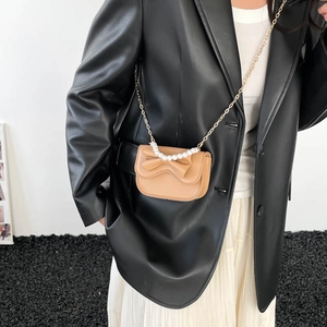 Mini khaki leather crossbody bag with a bow accent and pearl handle worn by a model