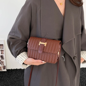 Brown woven leather crossbody bag with H-shaped gold buckle worn on a grey winter coat