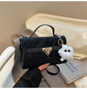 Detail of black textured crossbody bag featuring gold hardware and a cute plush charm