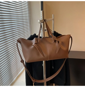 Detail of a brown leather tote bag featuring a unique knotted strap and dual shoulder straps