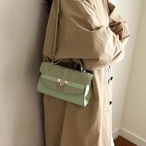 Sage green rectangular crossbody bag with gold buckle and chain, worn on a trench coat