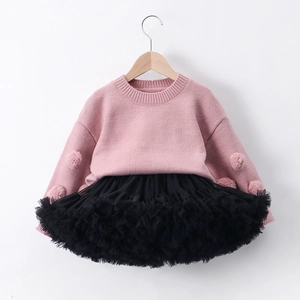 Detail of pink knitted sweater with pom-pom accents and black layered mesh tutu skirt