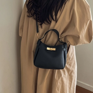 Chic black litchi grain leather bucket bag with gold lock worn by model with trench coat