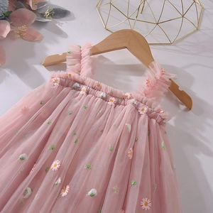 Détail d'une robe en tulle rose avec motifs de marguerites brodés et bretelles à volants