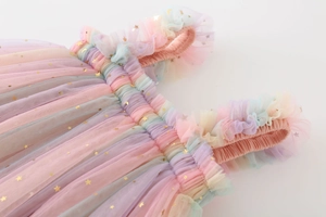 Detail of girls rainbow tulle dress featuring gold star prints and ruffled shoulders