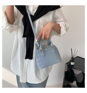 Detail of light blue crossbody shell bag with elegant quilted texture and gold hardware