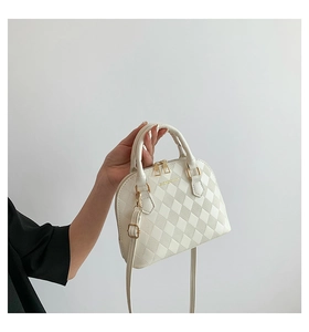 Detail of cream quilted shell handbag featuring gold logo and detachable shoulder strap