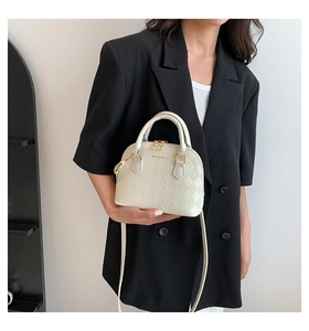 Detailed view of beige quilted shell bag with gold logo and dual zippers on black blazer