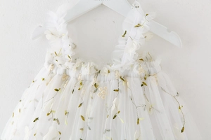 Detail of white tulle girls dress featuring green vine embroidery and 3D floral accents